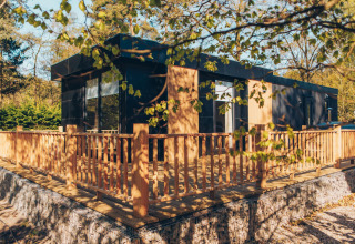Moderne lodge met houten terras en hekwerk in het groen, bij Veluwe park de Bosgraaf in Nederland.