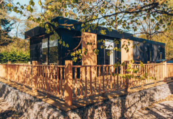 Lodge moderno con terrazza in legno e recinzione, immerso nel verde al parco Veluwe de Bosgraaf, Olanda.