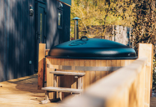 Bañera de hidromasaje de madera con tapa negra en la terraza de Valkhof met Hottub, Veluwe park de Bosgraaf, Países Bajos.