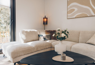 Salón moderno con sofá beige en L, cojines, mesa negra y florero en Valkhof met Hottub, Veluwe park de Bosgraaf, Países Bajos.
