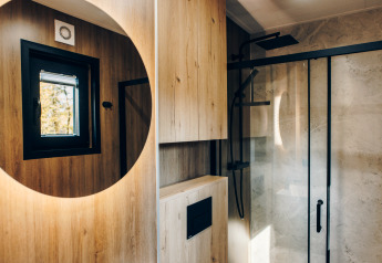 Modern bathroom with wooden walls, round mirror, and rain shower in Valkhof met Hottub, Veluwe park de Bosgraaf.