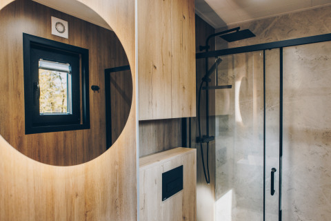 Baño moderno con paredes de madera, espejo redondo y ducha en Valkhof met Hottub del parque Veluwe de Bosgraaf.