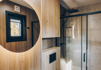 Moderne badkamer met houten wanden, rond spiegel en regendouche in Valkhof met Hottub, Veluwe park de Bosgraaf.