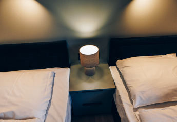 Two single beds with white sheets and a bedside lamp in Valkhof met Hottub at Veluwe park de Bosgraaf, Netherlands.