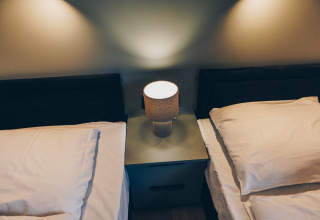 Twee eenpersoonsbedden met witte lakens en een nachtlampje bij Valkhof met Hottub in Veluwe park de Bosgraaf.