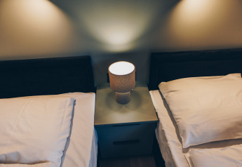 Twee eenpersoonsbedden met witte lakens en een nachtlampje bij Valkhof met Hottub in Veluwe park de Bosgraaf.