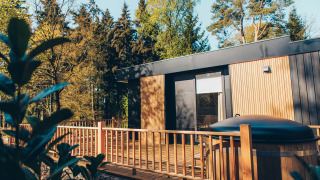 Moderne Valkhof-lodge met hottub en houten terras tussen bomen in Veluwe park de Bosgraaf, Nederland.