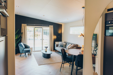 Moderne, gezellige woonkamer in een glampingaccommodatie met bank, eettafel en grote ramen.