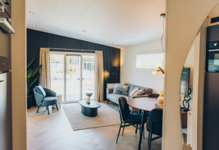 Modern, cozy living area in a glamping accommodation with sofa, dining table, and large windows.