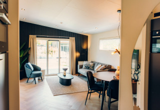 Knusse, moderne leefruimte in een glampingverblijf met sofa, eettafel en grote ramen.