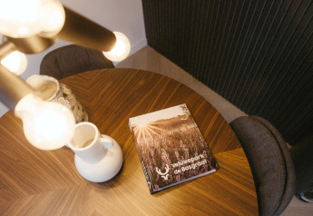 Mesa redonda de madera con libro sobre Veluwepark de Bosgraaf, jarra blanca y jarrón en glamping.