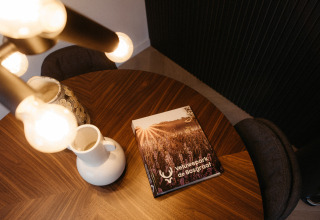 Round wooden table with a Veluwepark de Bosgraaf book, white jug, and vase in a glamping accommodation.