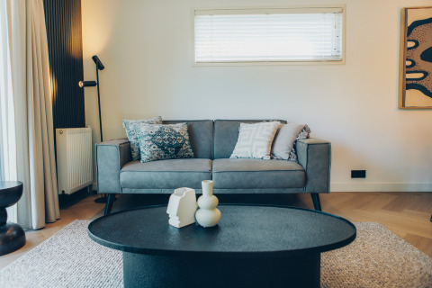 Modern living room at a glamping accommodation featuring a grey sofa, art on the wall, and chic table decor.