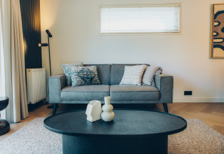 Modern living room at a glamping accommodation featuring a grey sofa, art on the wall, and chic table decor.