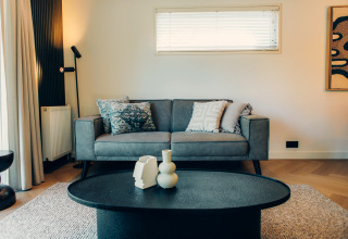 Modern living room at a glamping accommodation featuring a grey sofa, art on the wall, and chic table decor.