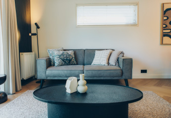 Salón moderno en un alojamiento glamping con sofá gris, mesa baja negra y decoración elegante de cojines.