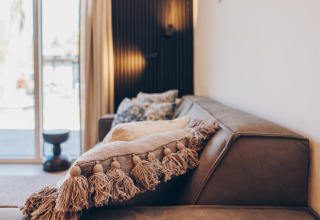 Gemütliches Wohnzimmer einer Glamping-Unterkunft mit braunem Sofa, stilvollen Kissen und Tageslicht.