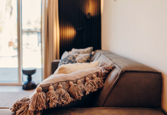 Moderne stue i et glamping-ophold med en brun sofa, pyntepude med kvaster og store vinduer.