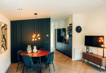 Alojamiento glamping moderno con comedor, cocina negra, televisor y lámparas decorativas elegantes.