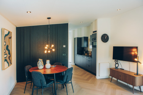 Moderne glamping accommodatie met eettafel, zwarte keuken, televisie en stijlvolle verlichting.