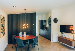 Modern glamping accommodation with a dining area, black kitchen, TV, and stylish lighting fixtures.