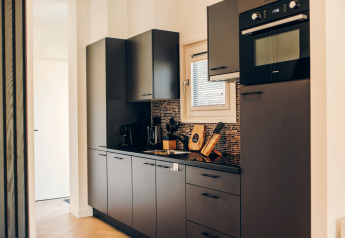 Cuisine de glamping moderne avec placards gris, four encastré, cafetière et crédence en mosaïque.