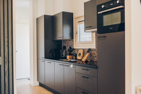 Cuisine de glamping moderne avec placards gris, four encastré, cafetière et crédence en mosaïque.