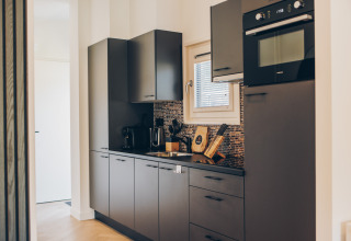 Cucina glamping moderna con mobili grigi, forno integrato, macchina da caffè e piastrelle a mosaico.