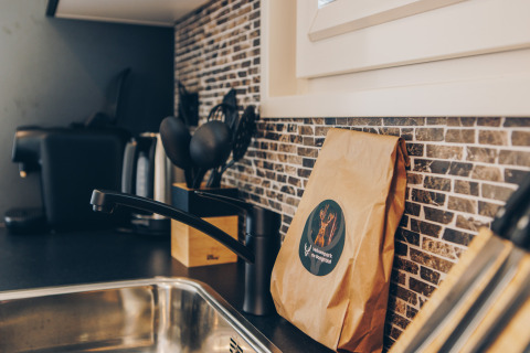 A glamping accommodation kitchen with a sink, coffee maker, utensils, and a brown paper bag on the counter.