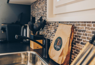A glamping accommodation kitchen with a sink, coffee maker, utensils, and a brown paper bag on the counter.