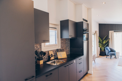 Modern kitchen in glamping accommodation with dark cabinets, utensils, sink, and a view to the lounge.