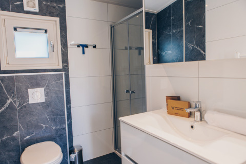 Salle de bain moderne dans un hébergement glamping avec douche, WC, lavabo, miroir et déco élégante.
