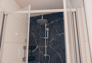 Cabine de douche moderne avec portes en verre et douche pluie prise dans un hébergement de glamping luxueux.
