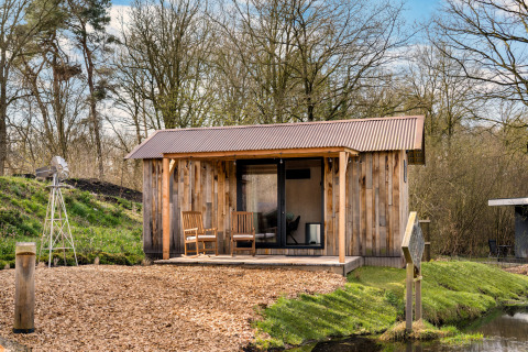 Cabaña de madera llamada 'Barn' en el camping Si-Es-An, rodeada de árboles y agua en los Países Bajos.