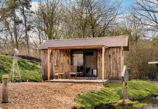 Cabaña de madera llamada 'Barn' en el camping Si-Es-An, rodeada de árboles y agua en los Países Bajos.