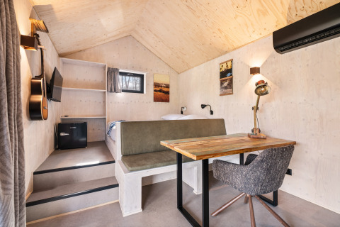 Interno della Nature house 'Barn' al campeggio Si-Es-An, Paesi Bassi, con letto, scrivania e chitarra.