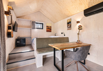 Interior de la casa 'Barn' en el camping Si-Es-An, Países Bajos, con cama, escritorio y guitarra.
