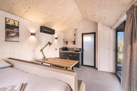 Interno in legno luminoso della casa Nature 'Barn' al campeggio Si-Es-An, angolo cottura, tavolo e finestra.