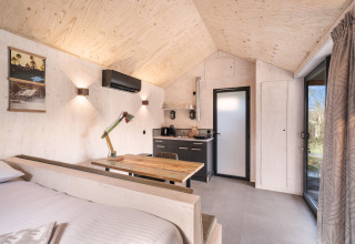 Interno in legno luminoso della casa Nature 'Barn' al campeggio Si-Es-An, angolo cottura, tavolo e finestra.