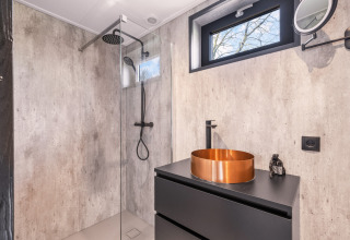 Baño moderno con lavabo de cobre y ducha tipo lluvia en Nature House 'Barn', camping Si-Es-An, Países Bajos.