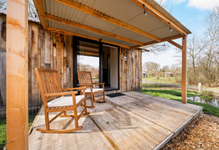 Wooden porch with rocking chairs at nature house 'Barn' in Campsite Si-Es-An, Netherlands, peaceful view.