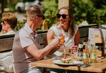 Zwei Personen genießen Getränke und Essen im Freien auf der Terrasse einer Glamping-Unterkunft.