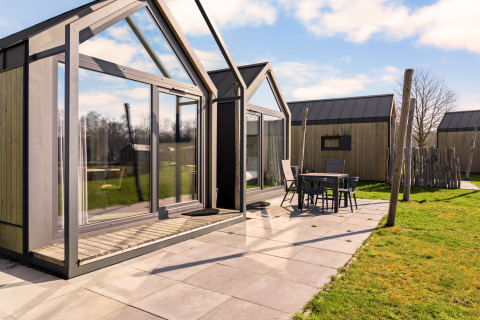 Outdoor view of a modern tiny house called Cosy House featuring large windows and a patio seating area.