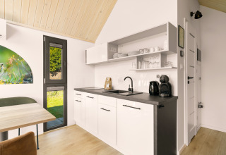 Angolo cottura moderno in una tiny house al campeggio Si-Es-An, Paesi Bassi, con mobili bianchi e legno.
