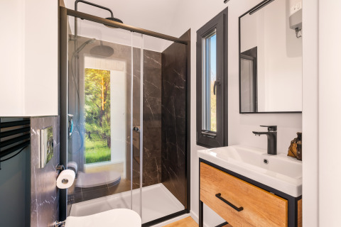 Bagno moderno in una tiny house al Campeggio Si-Es-An con doccia, finestra e mobile in legno.