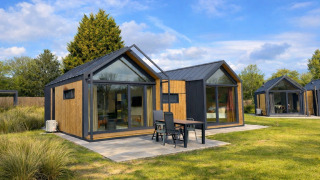 Cosy Lodge moderna con ampie vetrate, area esterna e prato verde sotto un cielo sereno e azzurro.