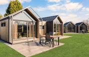 Moderni lodge con grandi vetrate e patio al campeggio Si-Es-An nei Paesi Bassi, giornata di sole.