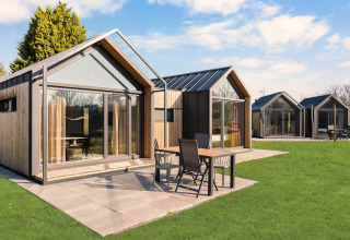 Moderni lodge con grandi vetrate e patio al campeggio Si-Es-An nei Paesi Bassi, giornata di sole.