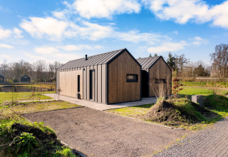 Modern wooden Cosy Lodge at Campsite Si-Es-An, Netherlands, with clear blue sky and natural surroundings.