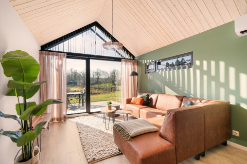 Bright living room in Cosy Lodge at Campsite Si-Es-An, Netherlands, with green wall, sofa, and garden view.